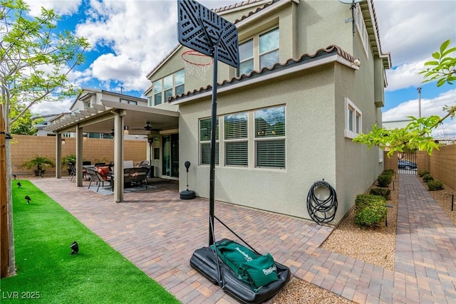 rear view of property featuring a patio, a ceiling fan, a fenced backyard, stucco siding, and a tiled roof