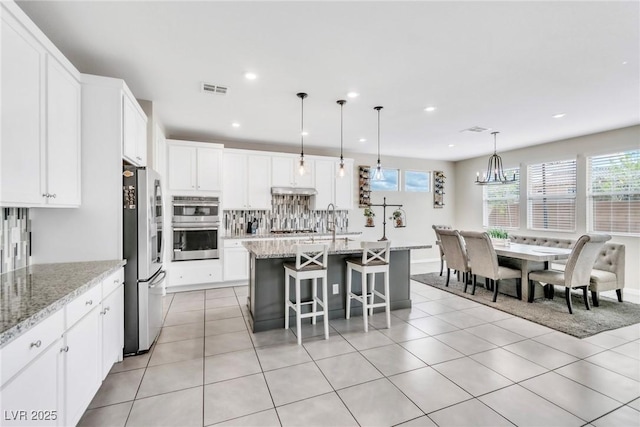 kitchen with tasteful backsplash, visible vents, appliances with stainless steel finishes, light tile patterned flooring, and white cabinets