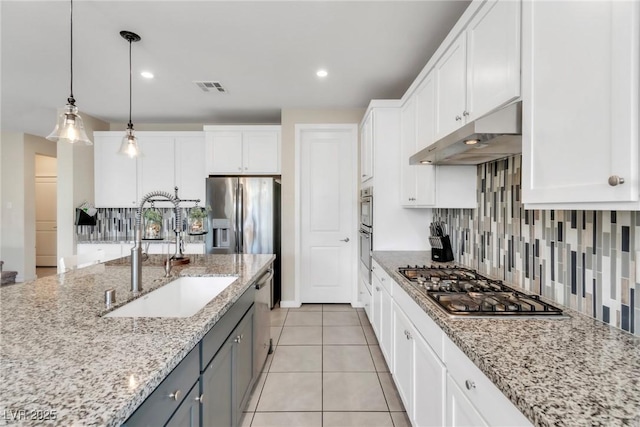 kitchen featuring visible vents, stainless steel appliances, a sink, under cabinet range hood, and backsplash