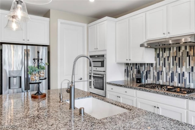 kitchen with a sink, decorative backsplash, white cabinets, under cabinet range hood, and appliances with stainless steel finishes