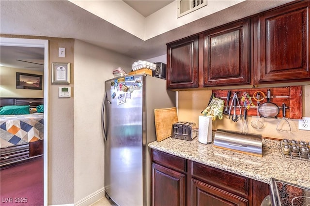 kitchen featuring light stone counters, visible vents, freestanding refrigerator, and baseboards