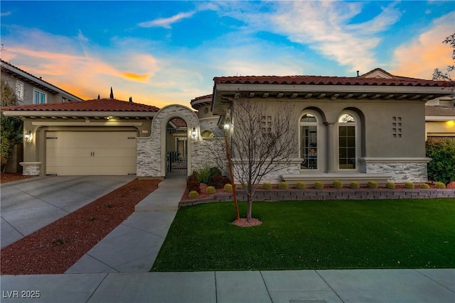 mediterranean / spanish-style house with concrete driveway, a lawn, stucco siding, stone siding, and an attached garage