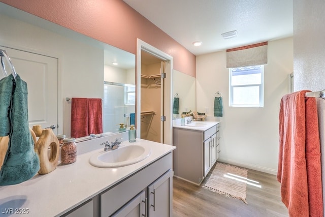 full bath with two vanities, a sink, wood finished floors, a shower stall, and a spacious closet