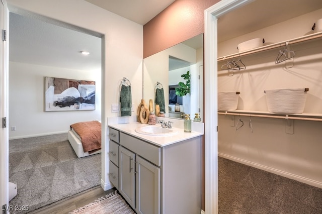 bathroom featuring connected bathroom, vanity, a walk in closet, and baseboards