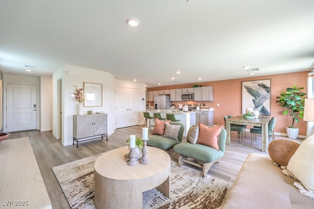 living room with recessed lighting, visible vents, light wood finished floors, and baseboards