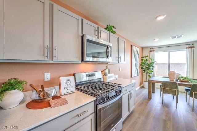 kitchen with visible vents, baseboards, light stone countertops, light wood-style floors, and stainless steel appliances