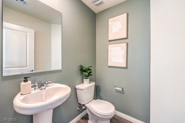 half bath featuring toilet, baseboards, visible vents, and a sink