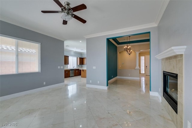 unfurnished living room with a tiled fireplace, ceiling fan with notable chandelier, crown molding, decorative columns, and baseboards