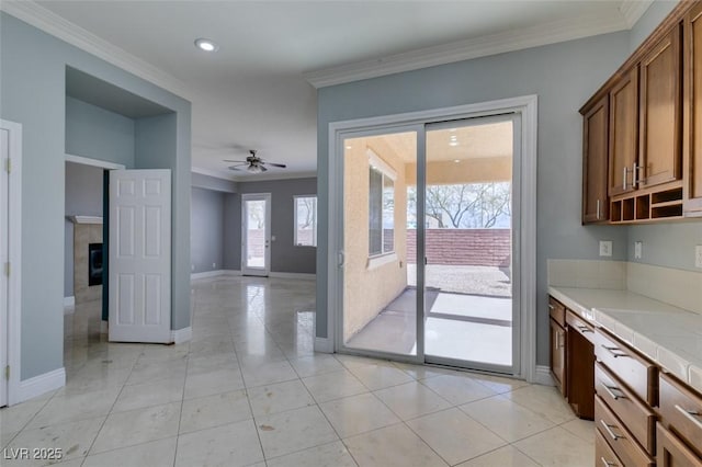 kitchen with tile countertops, light tile patterned floors, baseboards, ceiling fan, and crown molding