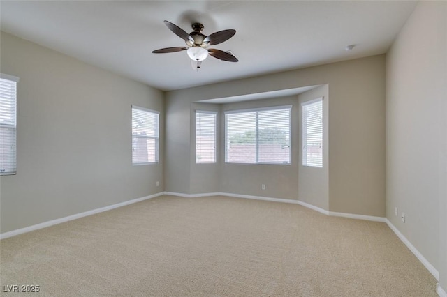 spare room featuring light colored carpet, baseboards, and ceiling fan