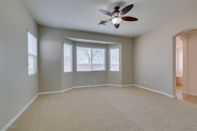 unfurnished room featuring a wealth of natural light, arched walkways, light carpet, and ceiling fan