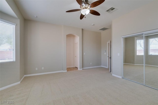 unfurnished bedroom featuring arched walkways, visible vents, light carpet, and baseboards