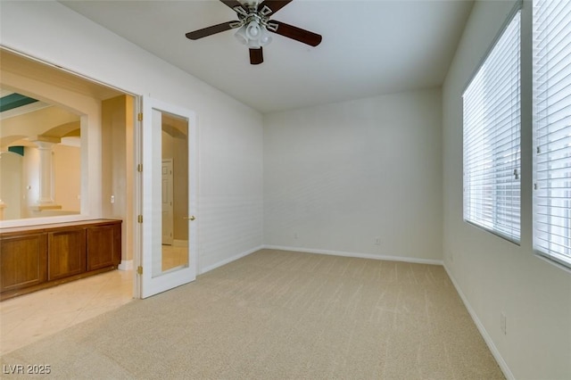 unfurnished room featuring arched walkways, baseboards, light colored carpet, ceiling fan, and ornate columns