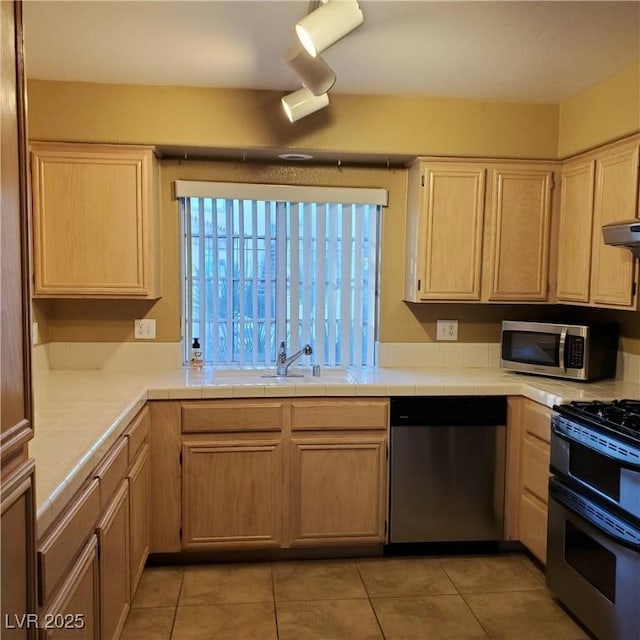 kitchen with a sink, tile countertops, appliances with stainless steel finishes, light tile patterned floors, and extractor fan