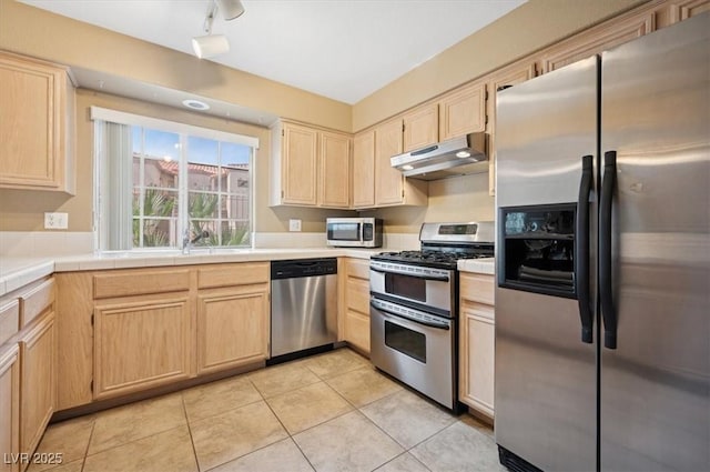 kitchen featuring stainless steel appliances, under cabinet range hood, light brown cabinets, and tile counters