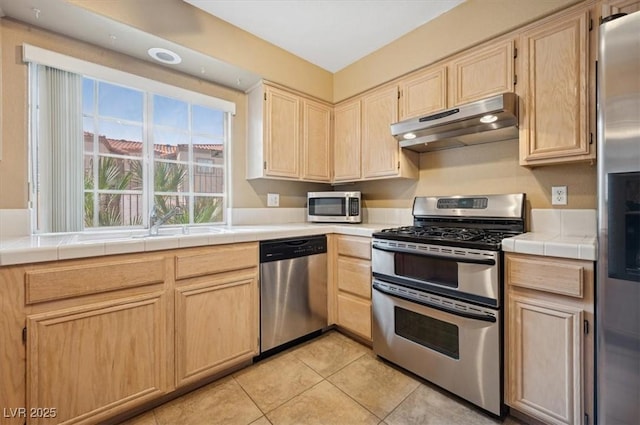 kitchen featuring stainless steel appliances, tile counters, light tile patterned flooring, light brown cabinets, and under cabinet range hood