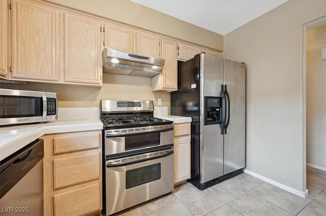 kitchen featuring stainless steel appliances, tile counters, under cabinet range hood, and light brown cabinets