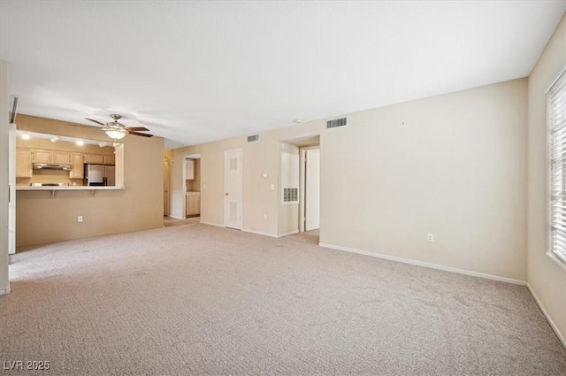 unfurnished living room featuring visible vents, light colored carpet, baseboards, and ceiling fan