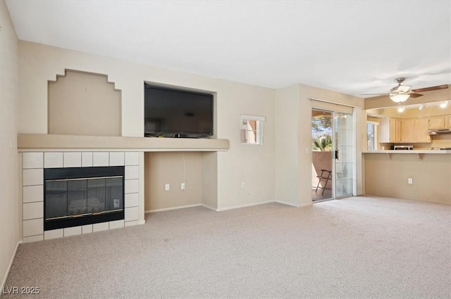 unfurnished living room featuring a tiled fireplace, carpet flooring, baseboards, and a ceiling fan
