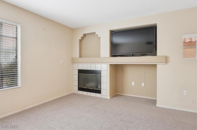 unfurnished living room featuring a healthy amount of sunlight, a tile fireplace, baseboards, and carpet floors