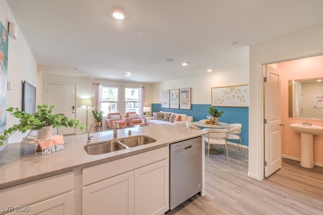 kitchen with light stone countertops, open floor plan, dishwasher, white cabinets, and a sink