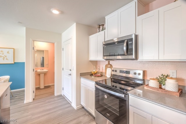 kitchen with baseboards, light wood-type flooring, appliances with stainless steel finishes, white cabinetry, and a sink