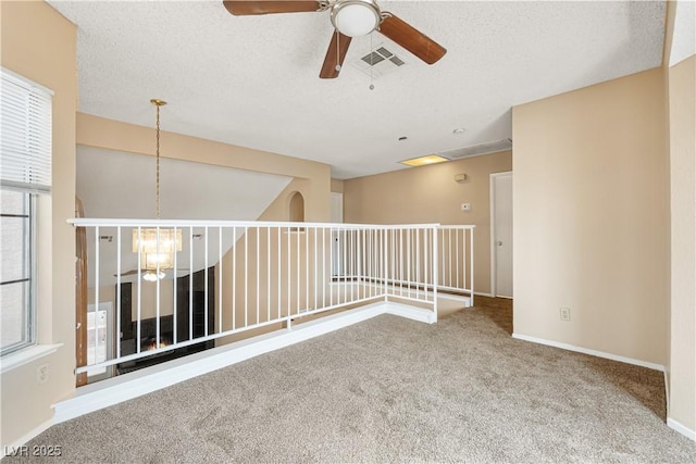 carpeted spare room featuring a wealth of natural light, visible vents, ceiling fan with notable chandelier, and a textured ceiling