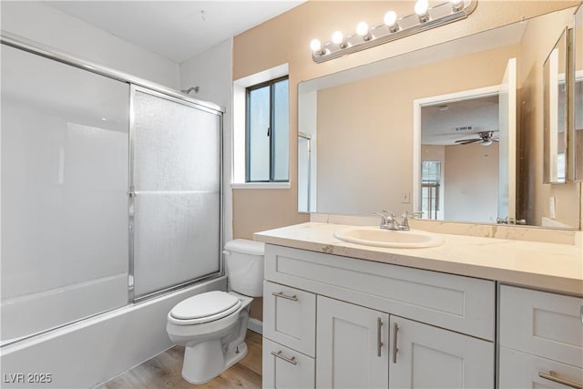 full bath featuring toilet, wood finished floors, combined bath / shower with glass door, vanity, and a ceiling fan