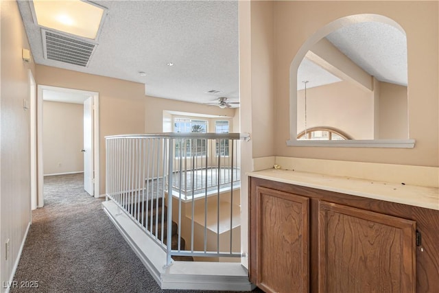 hall with visible vents, a textured ceiling, arched walkways, carpet, and baseboards