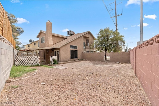 rear view of house with central AC, stucco siding, a chimney, and a fenced backyard