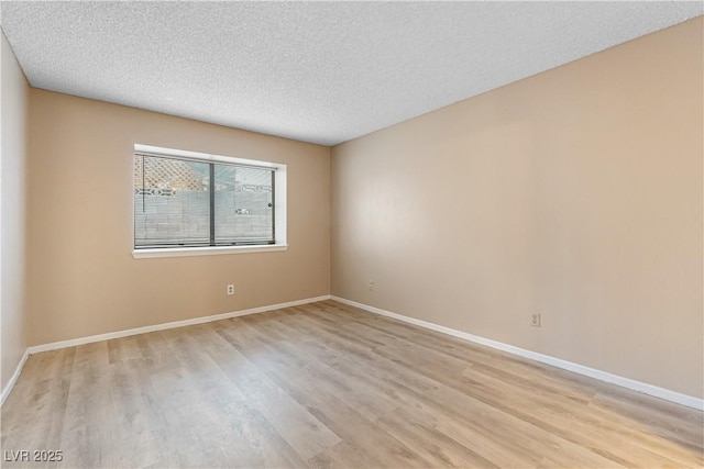 empty room with light wood-style floors, baseboards, and a textured ceiling