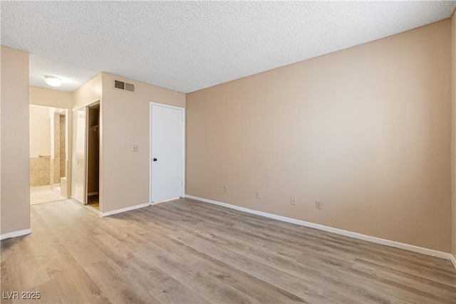 spare room with visible vents, baseboards, light wood-style floors, and a textured ceiling