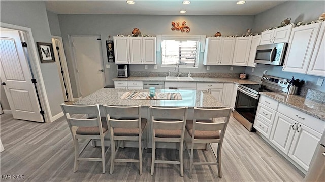 kitchen featuring a kitchen bar, light wood-style flooring, appliances with stainless steel finishes, white cabinets, and a sink