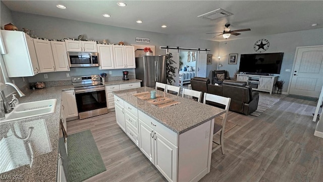 kitchen with visible vents, a kitchen island, a sink, appliances with stainless steel finishes, and white cabinetry