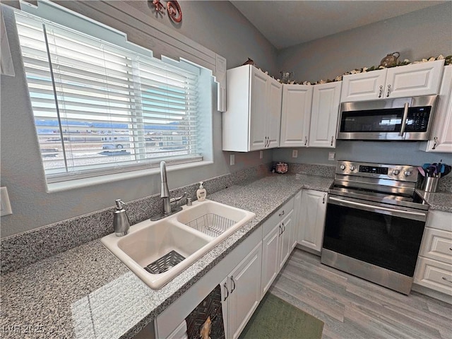 kitchen featuring appliances with stainless steel finishes, white cabinetry, light countertops, and a sink