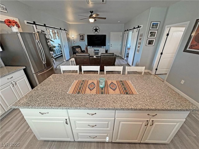 kitchen with a barn door, light stone countertops, freestanding refrigerator, and ceiling fan