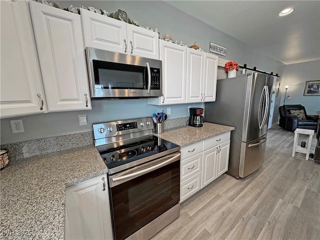 kitchen with light stone counters, light wood-style flooring, stainless steel appliances, white cabinetry, and a barn door