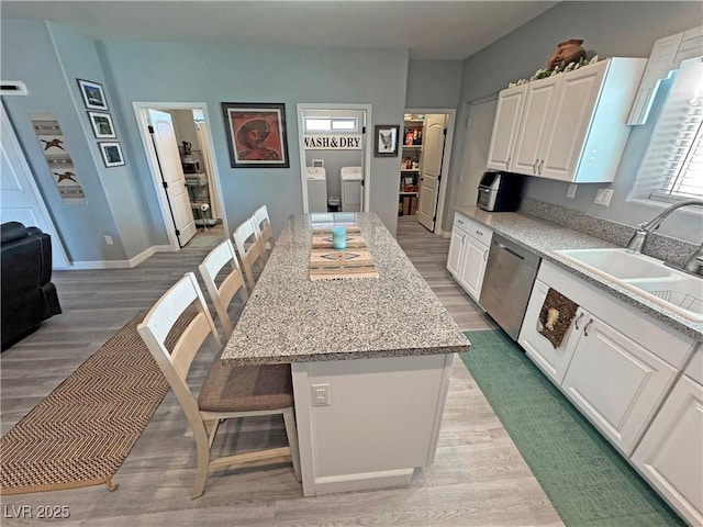 kitchen featuring washer and dryer, a sink, white cabinets, dishwasher, and light wood-type flooring