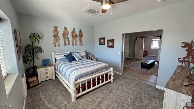 carpeted bedroom with a barn door, baseboards, visible vents, and ceiling fan