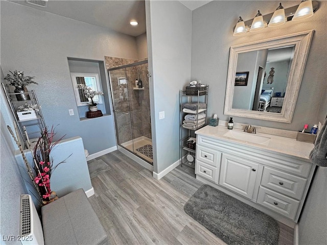 bathroom featuring visible vents, a stall shower, wood finished floors, baseboards, and vanity