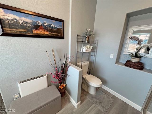 bathroom with toilet, radiator heating unit, baseboards, and wood finished floors