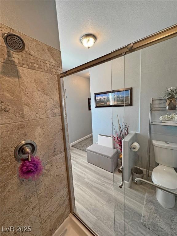 bathroom featuring a textured ceiling, toilet, and tiled shower