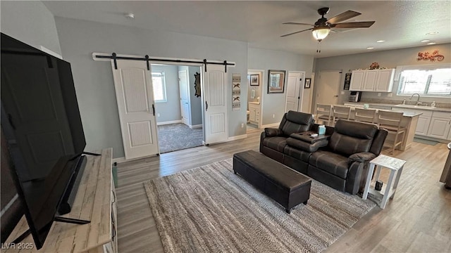 living area featuring ceiling fan, baseboards, light wood-type flooring, a barn door, and recessed lighting