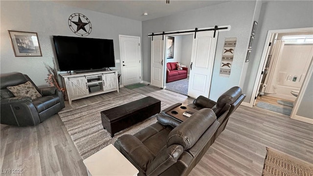 living room featuring light wood-type flooring, a barn door, and baseboards