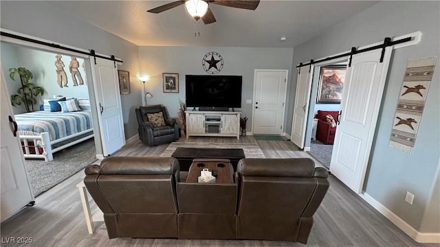 living area featuring a barn door, wood finished floors, baseboards, and ceiling fan