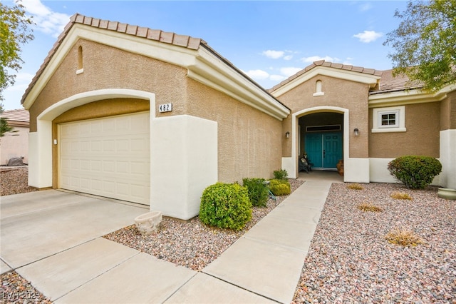 view of exterior entry featuring stucco siding, a garage, concrete driveway, and a tiled roof