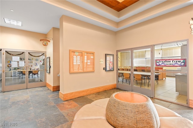 interior space with visible vents, baseboards, a tray ceiling, french doors, and a towering ceiling