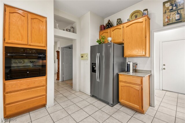 kitchen with light tile patterned floors, black oven, light countertops, and stainless steel refrigerator with ice dispenser