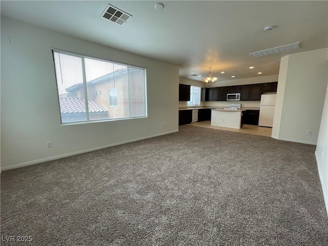 unfurnished living room featuring an inviting chandelier, baseboards, visible vents, and light carpet