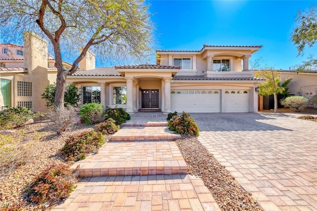 mediterranean / spanish home with a tiled roof, stucco siding, a chimney, decorative driveway, and an attached garage